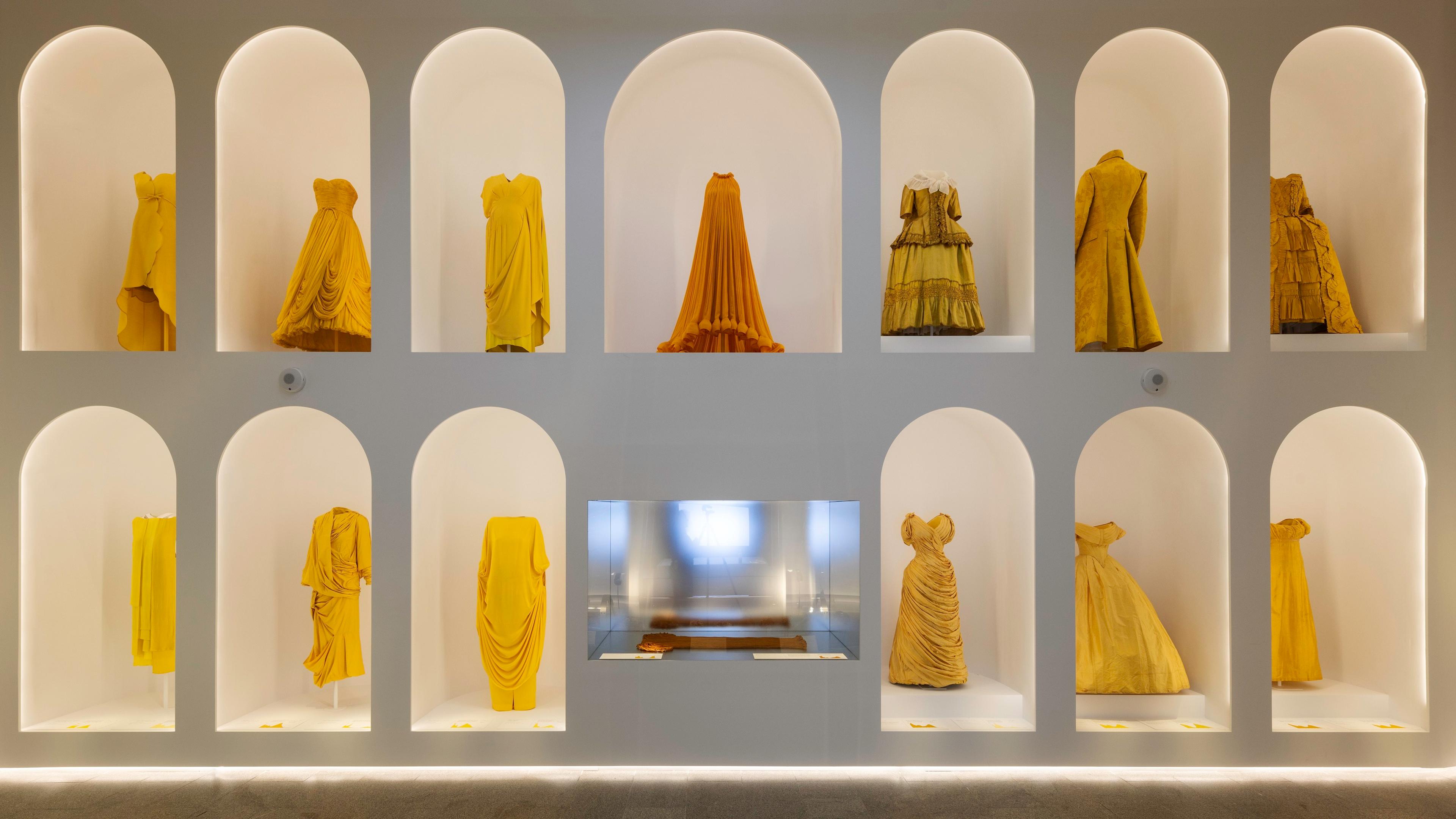 A collection of elegant yellow dresses displayed in arched niches, showcasing diverse styles and textures against a minimalist backdrop.
