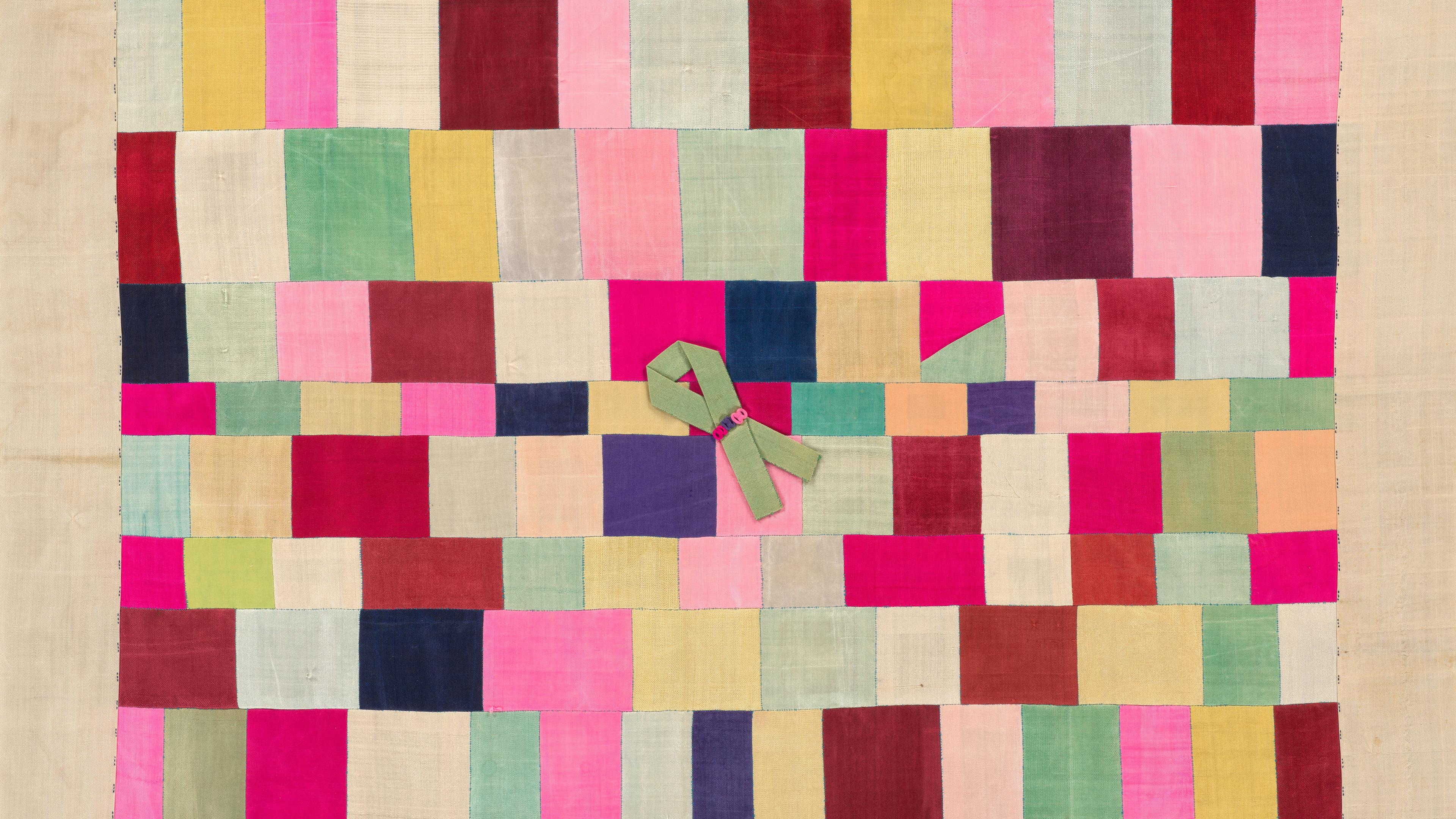 Colorful quilt made of rectangular silk patches in various shades. A green ribbon with pink buttons is sewn near the center.