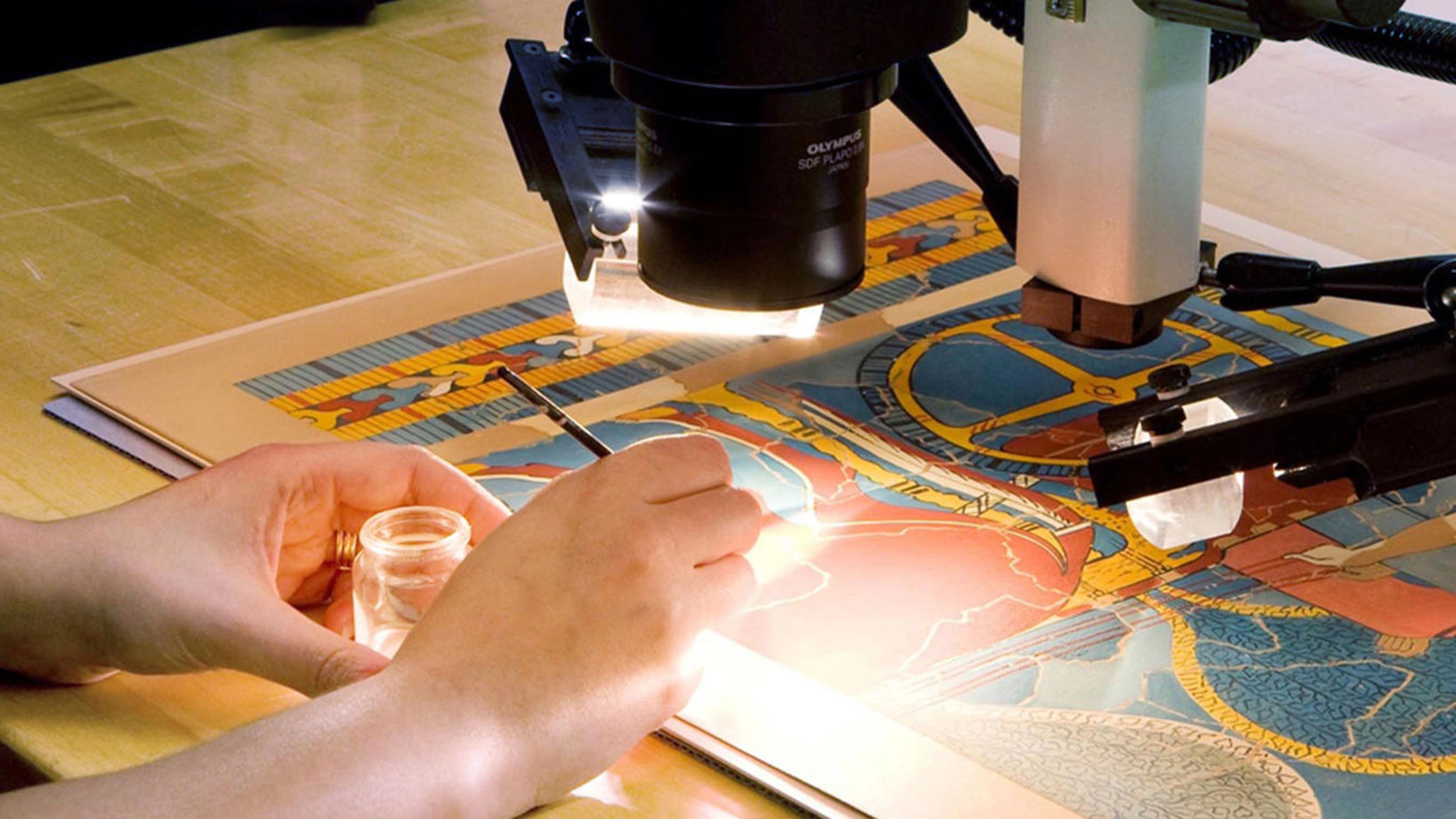 A woman looking through a telescope, examining a colorful work of art on paper
