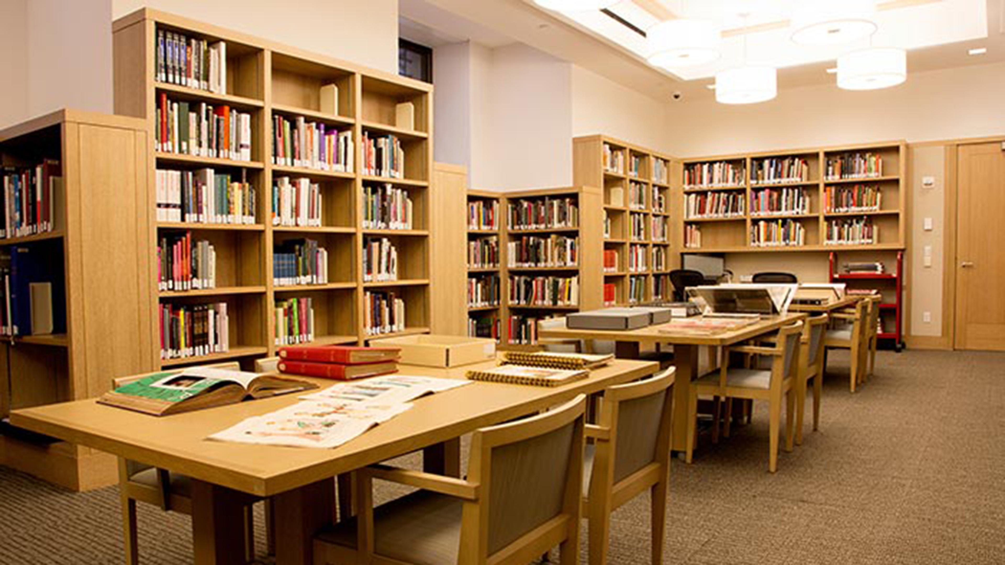 A bright, modern, blonde wood library lined with shelves of books and tables with comfortable chairs