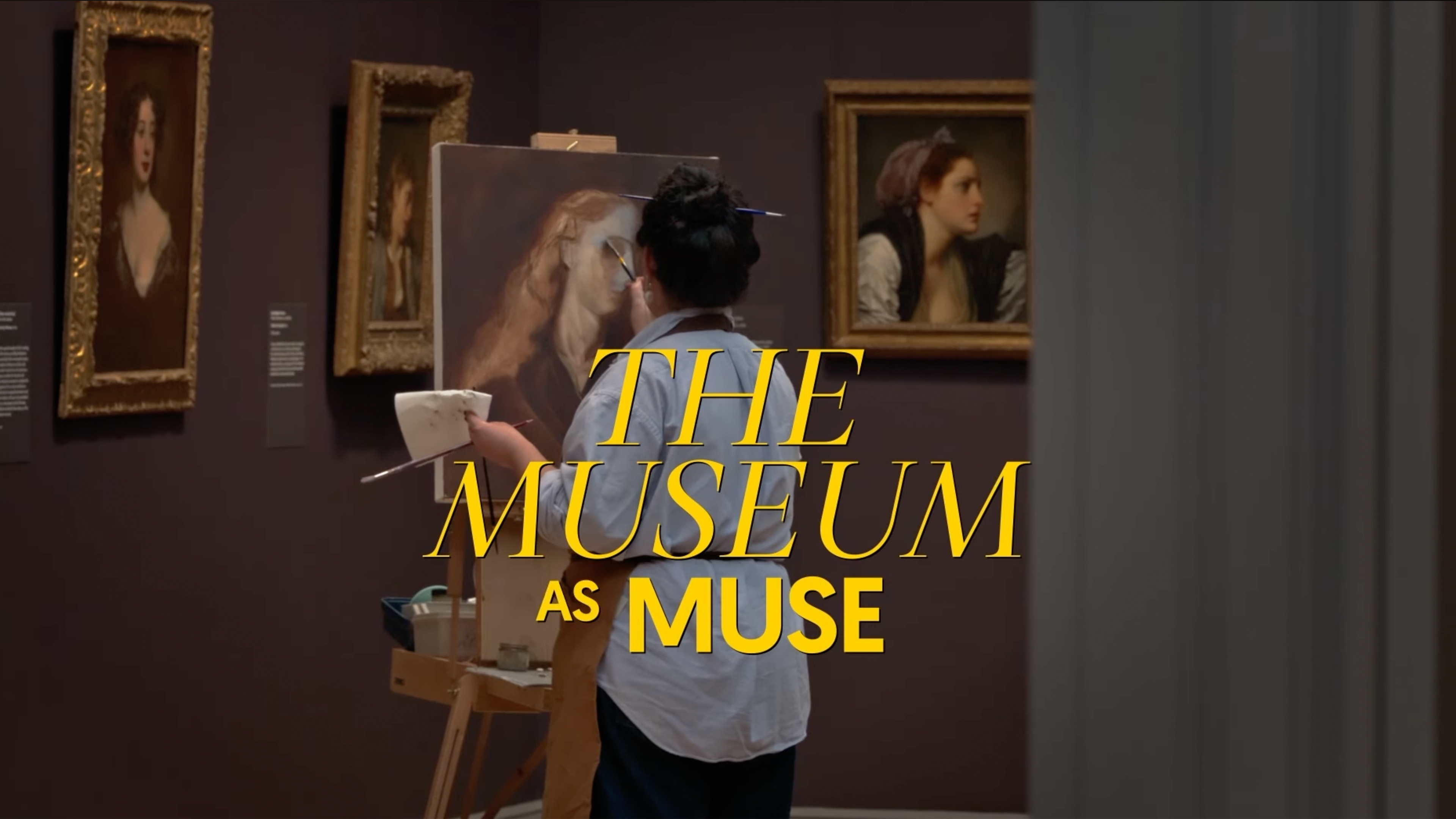 In a dim museum gallery, an artist stands at an easel painting a large portrait on canvas, holding a palette. Framed portraits hang on the dark wall behind them. Bold yellow text over the scene reads ‘THE MUSEUM AS MUSE.’