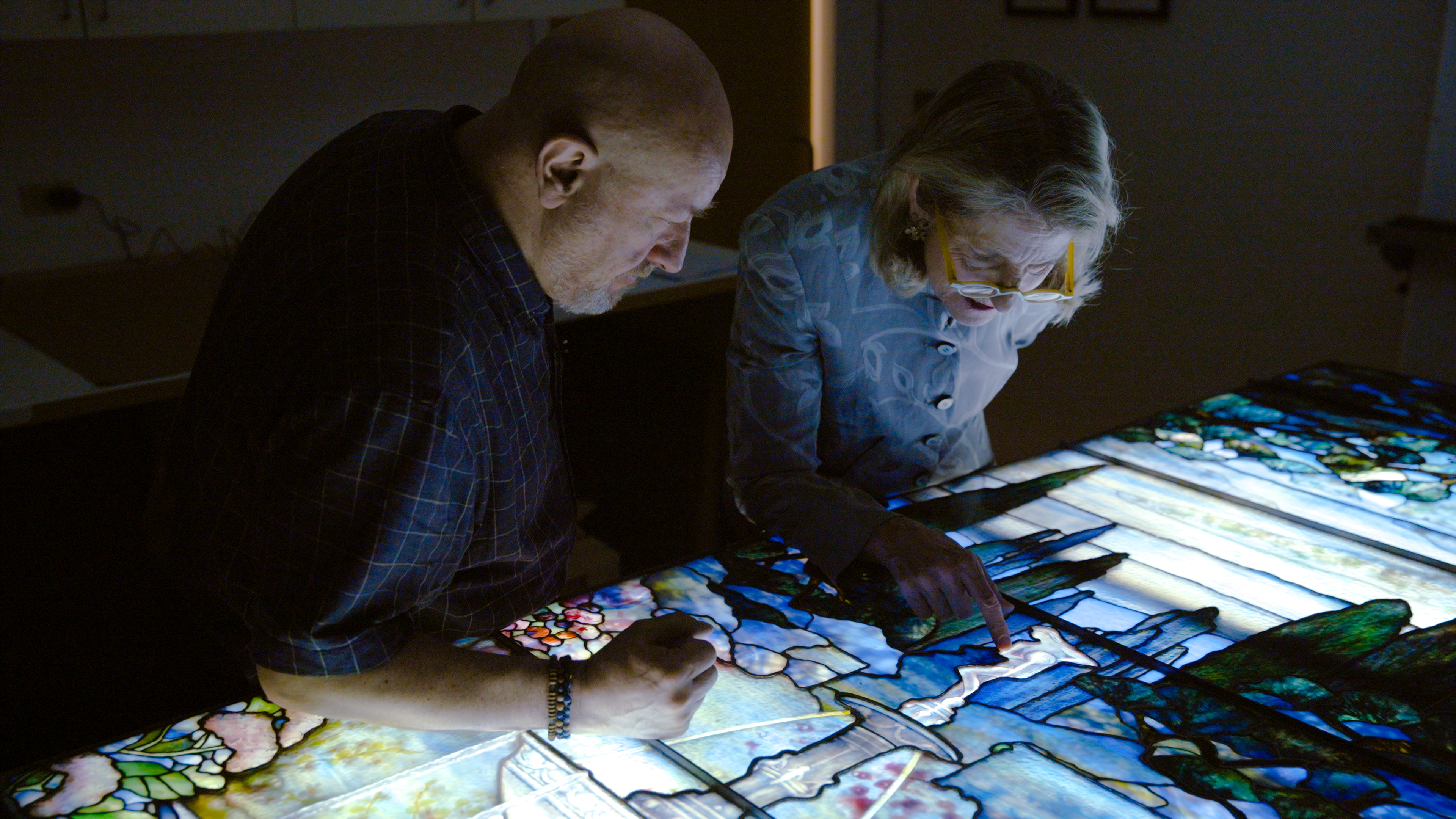 Man and woman looking down observing a stain glass window.